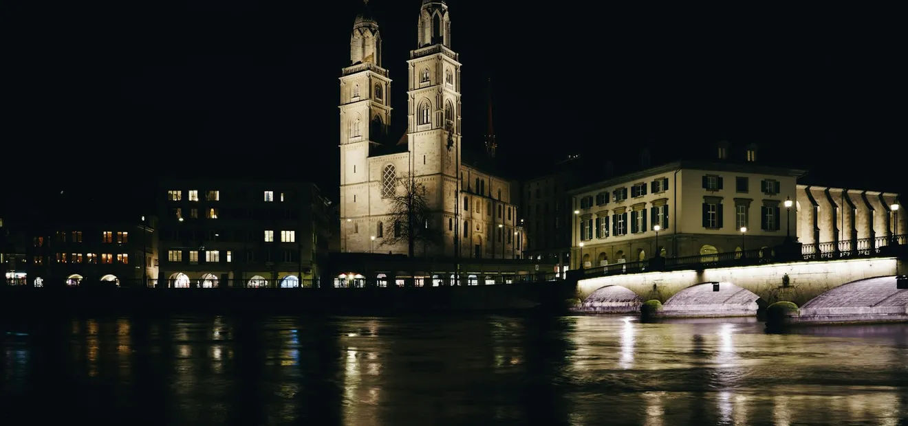 The twin towers of the Grossmünster and a floodlit bridge, seen across the Limmat at night.