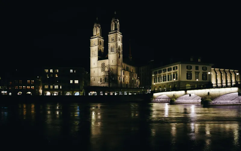 The twin towers of the Grossmünster and a floodlit bridge, seen across the Limmat at night.