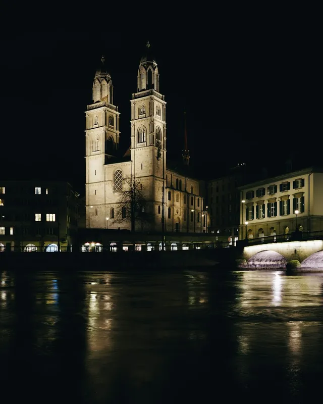 The twin towers of the Grossmünster and a floodlit bridge, seen across the Limmat at night.