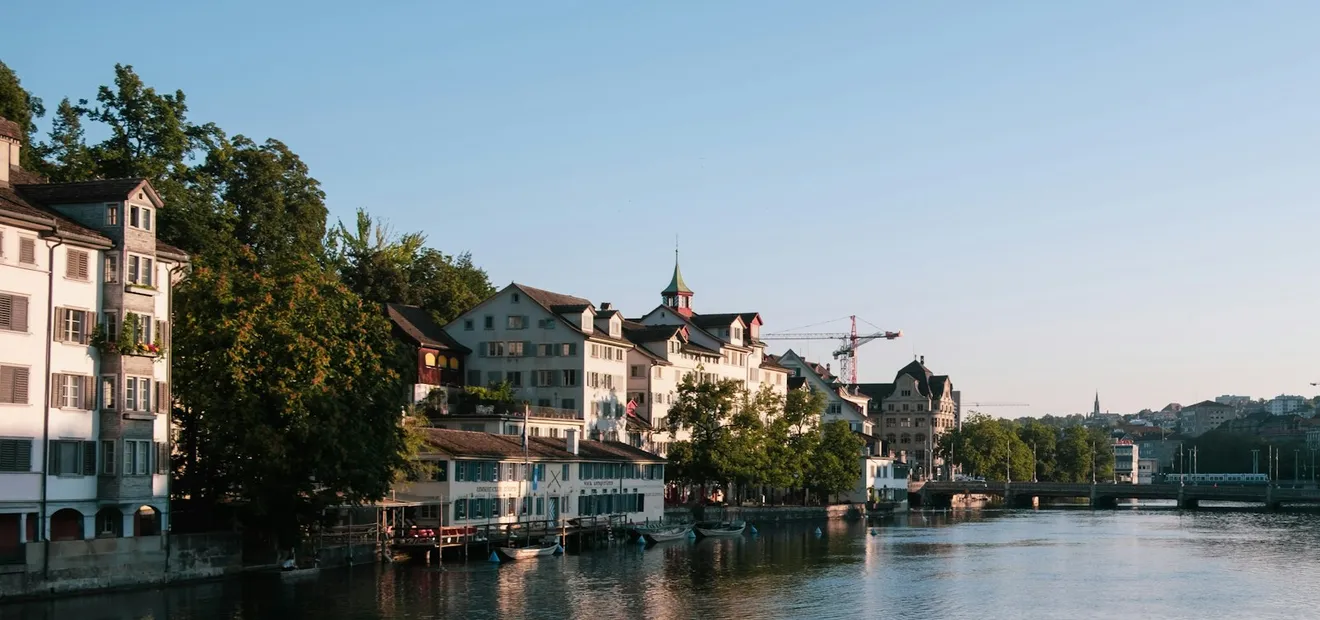 Houses along the Limmat in low evening light, with a bridge in the distance.